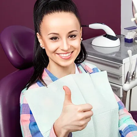 A young woman in a dental exam chair giving a thumbs up
